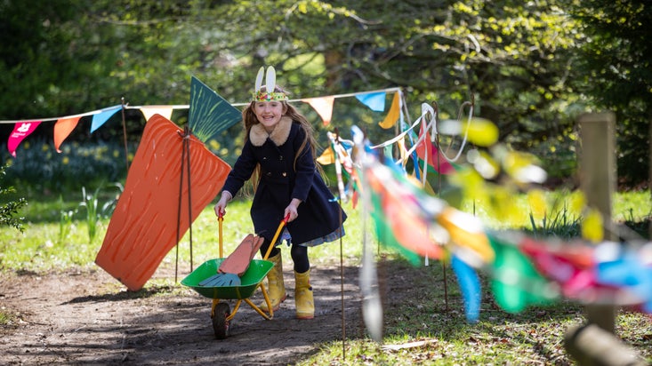 A young girl in wellies pushing a wheelbarrow next to colourful bunting
